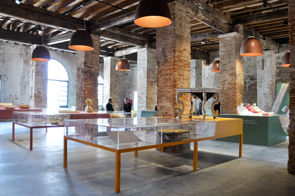 Teche e tavoli espositivi tra le colonne in mattoni dell'Arsenale di Venezia