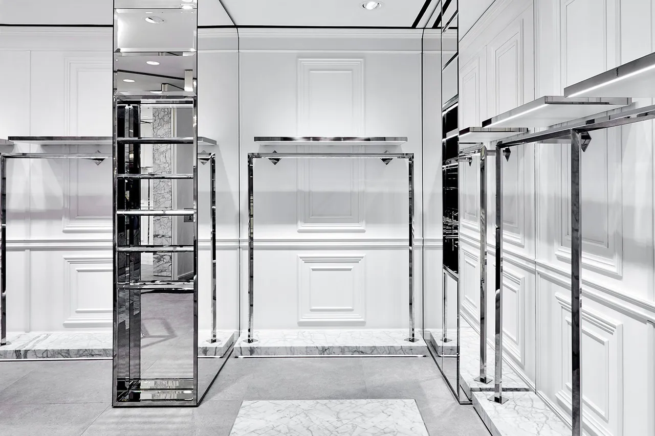 Interno di boutique con boiserie bianca, specchi e appenderie in acciaio